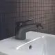 Schwarze Bidetarmatur von Ideal Standard mit einem Hebel und einem ausziehbaren Auslauf, montiert auf einem weißen Waschbecken vor einem gefliesten Hintergrund.